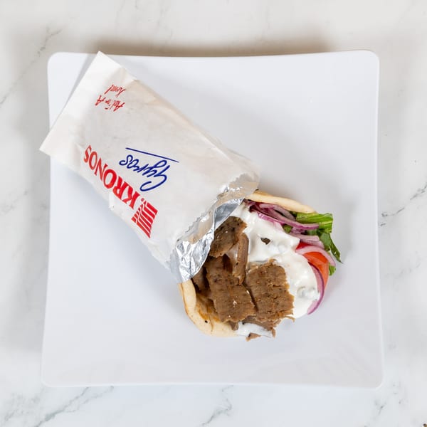 Kronos Gyros with meat, lettuce, tomato, onion, and tzatziki sauce on a white plate.