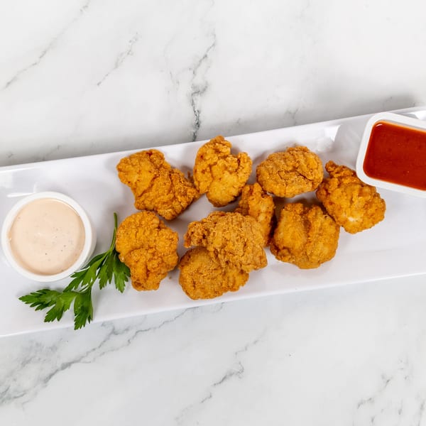 Crispy fried chicken nuggets on a white rectangular plate with two dipping sauces and parsley.