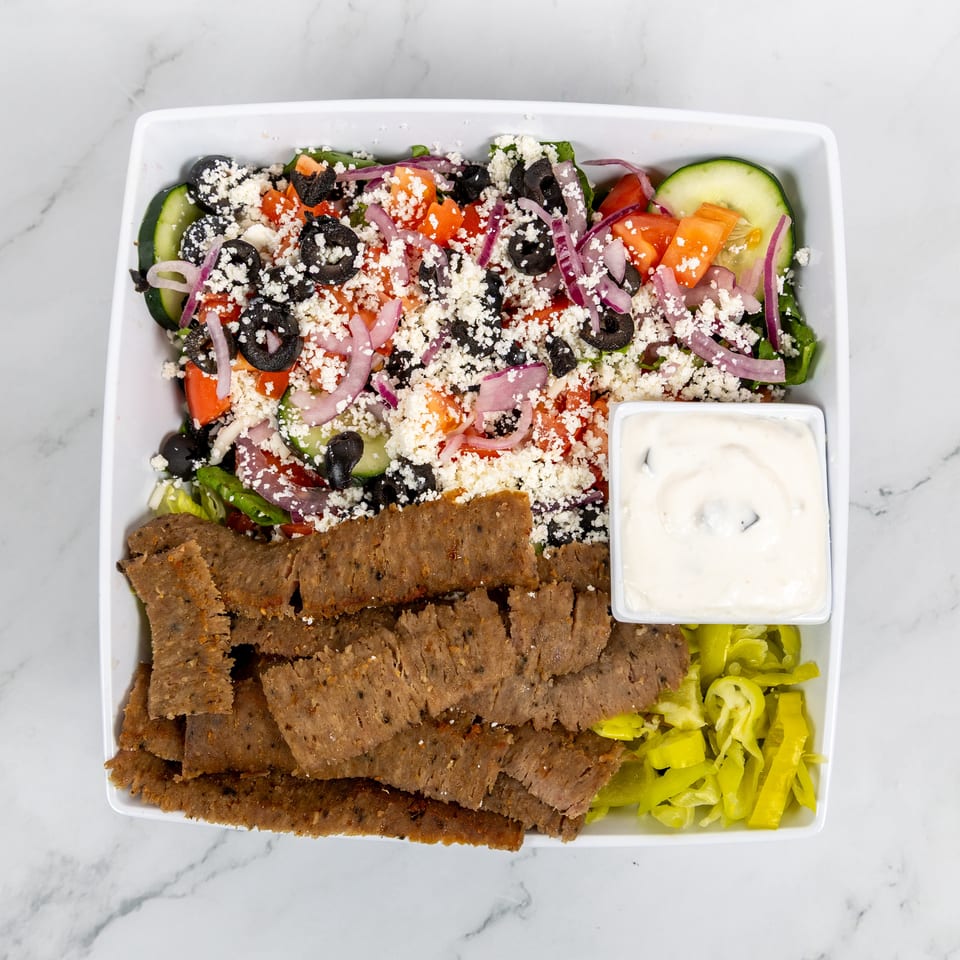 Overhead view of a gyro platter with sliced meat, Greek salad, tzatziki, and pickled peppers.