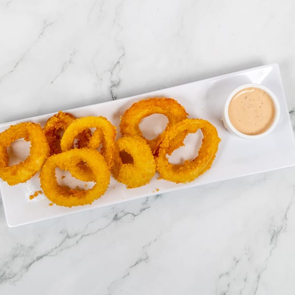 Golden-brown onion rings and a small cup of dipping sauce on a white rectangular plate.