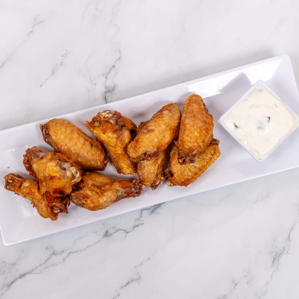 Golden-brown fried chicken wings and a small dish of creamy dipping sauce on a white rectangular plate.