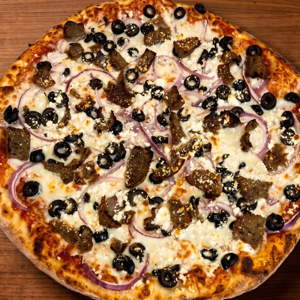 A whole pizza with white cheese, black olives, red onions, and gyro meat on a wooden table.