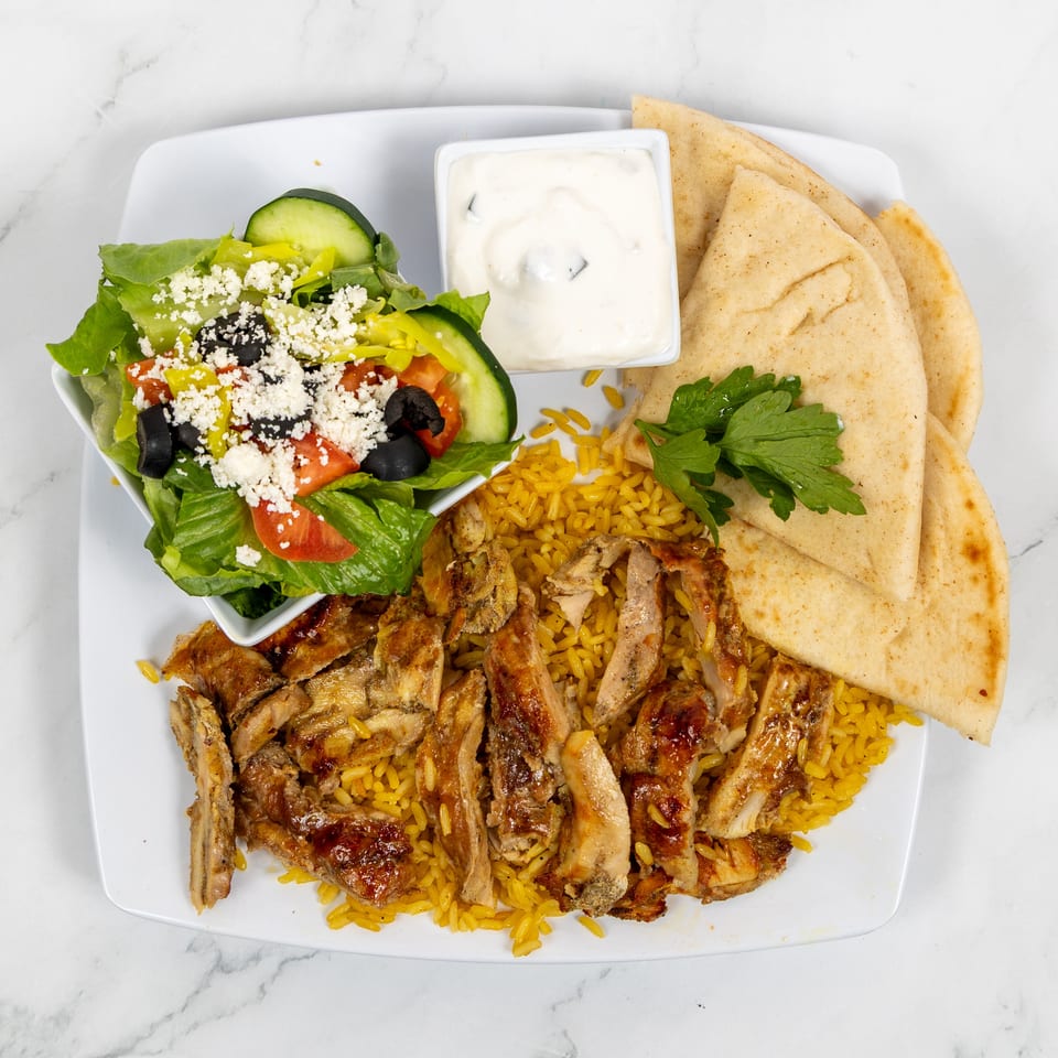 Chicken and rice platter with a side salad, pita bread, and white sauce on a white plate.