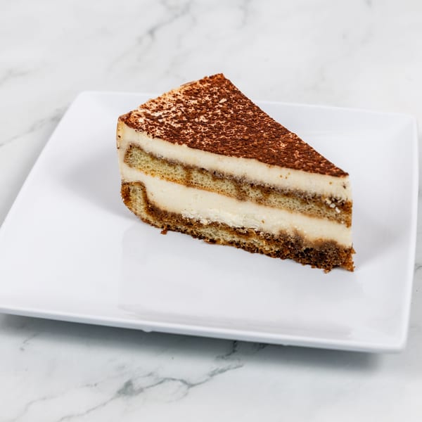 A slice of tiramisu with layers of cream and cake, dusted with cocoa powder, on a white plate.