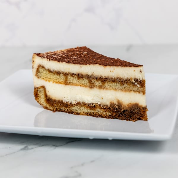 A slice of tiramisu with layers of ladyfingers, cream, and cocoa powder on a white plate.
